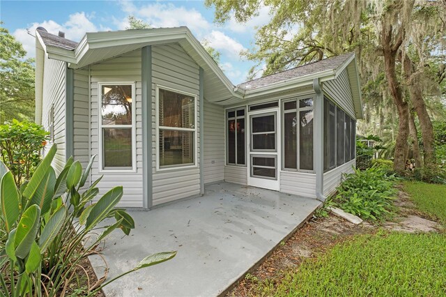 rear view of property featuring a shingled roof, a patio area, and a sunroom