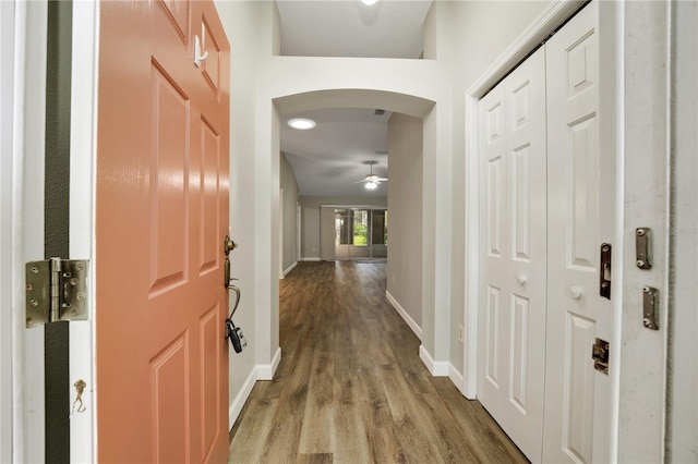 hall with arched walkways, baseboards, and wood finished floors