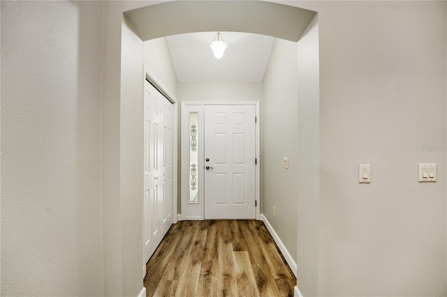 doorway featuring arched walkways, baseboards, and wood finished floors