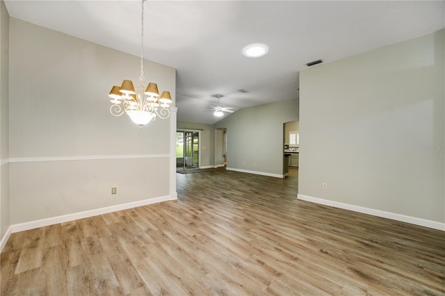 empty room featuring ceiling fan with notable chandelier, baseboards, wood finished floors, vaulted ceiling, and visible vents
