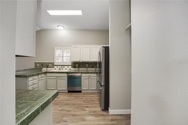 kitchen with backsplash, tile countertops, light wood finished floors, stainless steel appliances, and white cabinetry