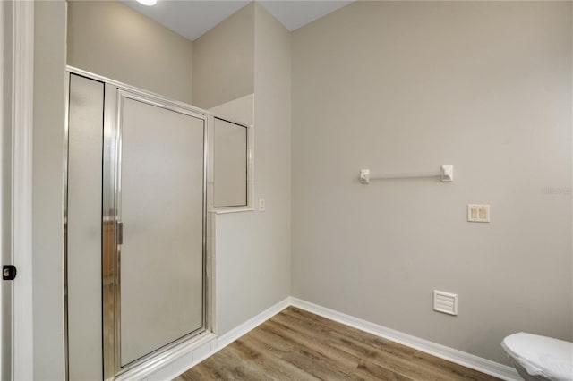 bathroom with wood finished floors, baseboards, a stall shower, and toilet