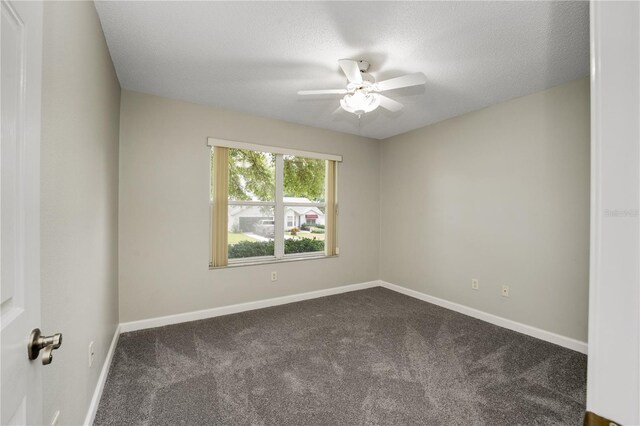 empty room featuring a ceiling fan, baseboards, dark carpet, and a textured ceiling