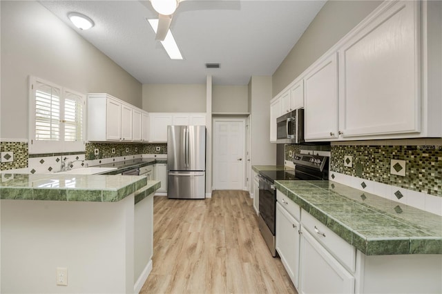 kitchen featuring decorative backsplash, visible vents, appliances with stainless steel finishes, light wood-type flooring, and tile counters