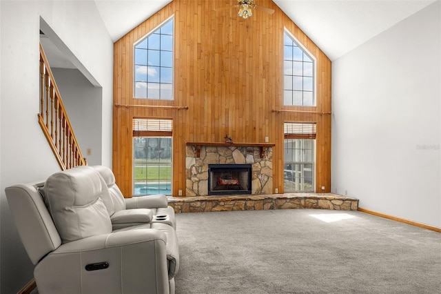 carpeted living room featuring a fireplace, high vaulted ceiling, wooden walls, and ceiling fan