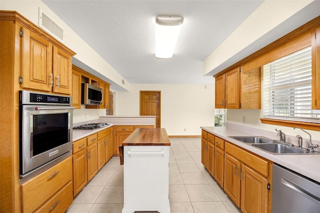 kitchen featuring sink, stainless steel appliances, a textured ceiling, light tile patterned flooring, and wood counters