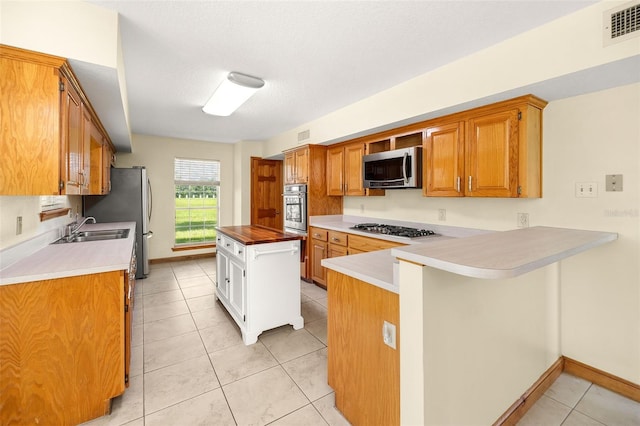 kitchen with sink, light tile patterned floors, appliances with stainless steel finishes, a textured ceiling, and kitchen peninsula