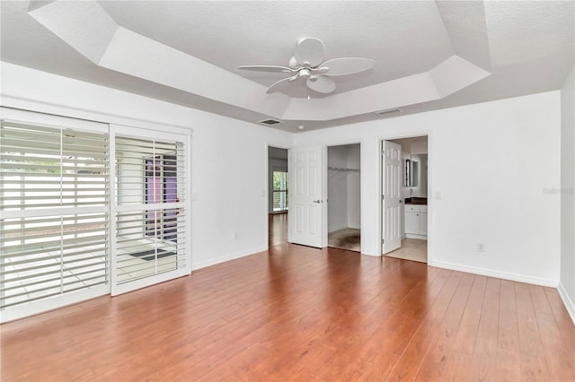 unfurnished bedroom with ceiling fan, a spacious closet, tile patterned flooring, connected bathroom, and a tray ceiling