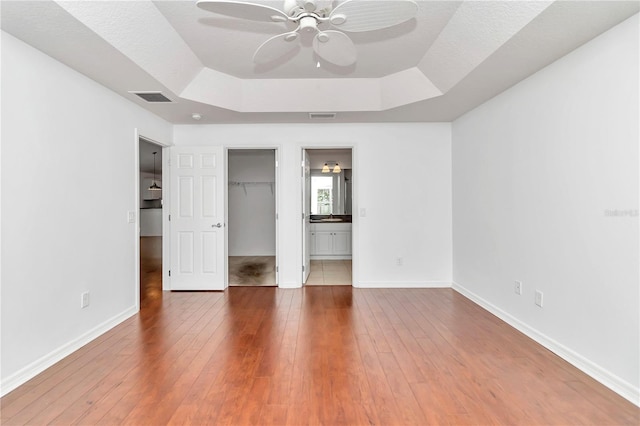 unfurnished bedroom featuring tile patterned floors, ceiling fan, a walk in closet, and a tray ceiling