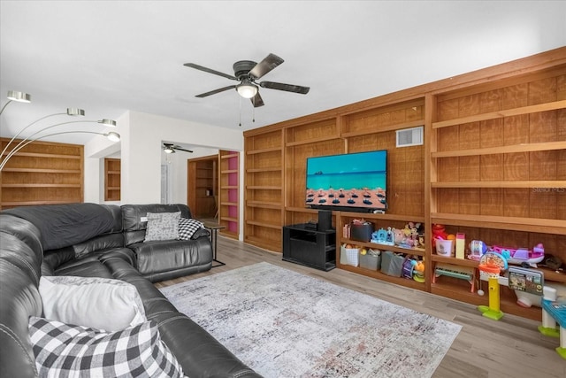 living room featuring built in shelves, ceiling fan, and light hardwood / wood-style flooring