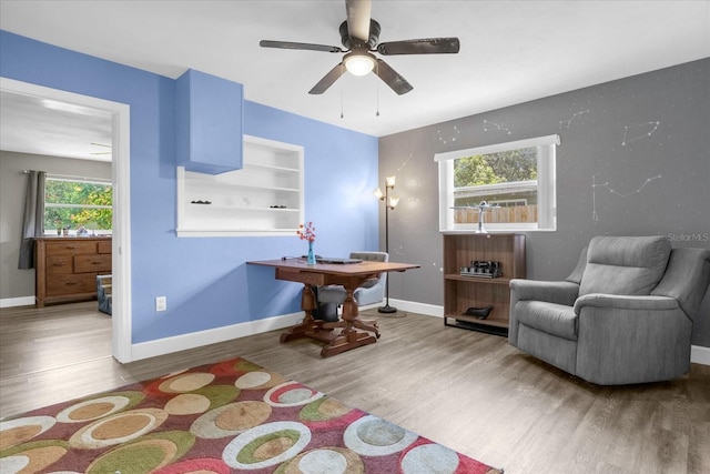 sitting room with wood-type flooring, built in features, and ceiling fan