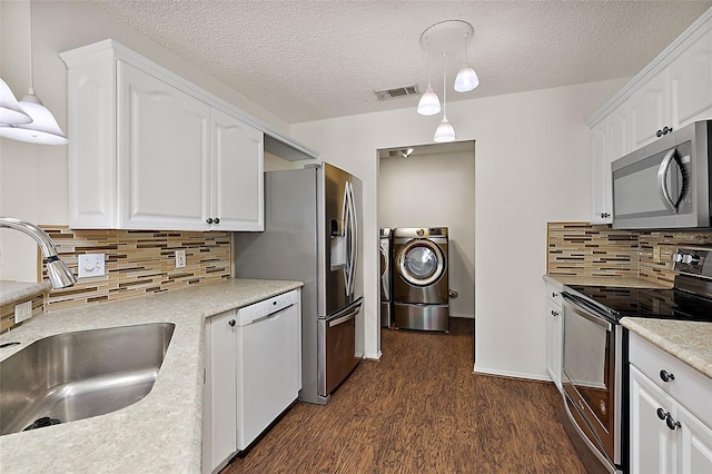 kitchen featuring white cabinets, sink, hanging light fixtures, washing machine and dryer, and stainless steel appliances