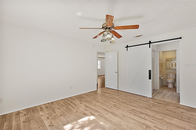 unfurnished room with ceiling fan, a barn door, a textured ceiling, and light hardwood / wood-style flooring