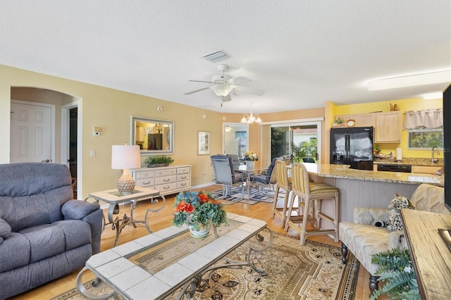 living room with ceiling fan with notable chandelier, a wealth of natural light, a textured ceiling, and light hardwood / wood-style floors