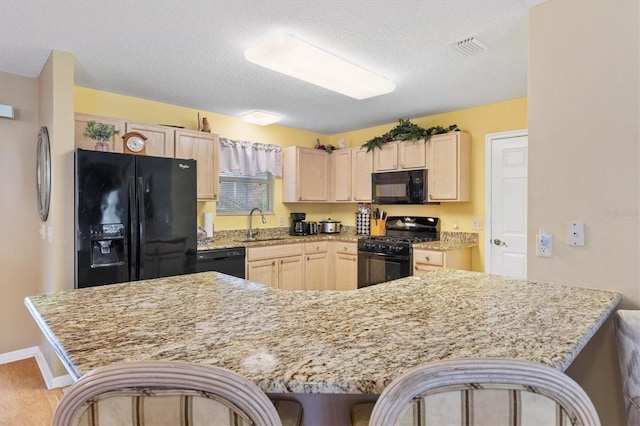 kitchen with sink, a kitchen breakfast bar, black appliances, light stone countertops, and a textured ceiling