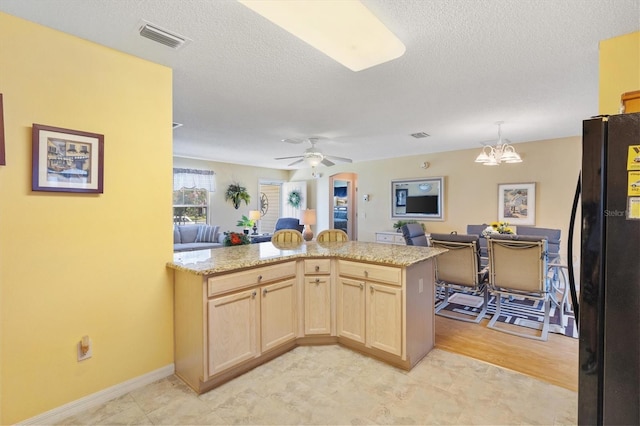 kitchen with ceiling fan with notable chandelier, black refrigerator, light brown cabinets, and a textured ceiling