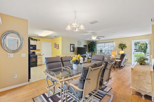 dining space with ceiling fan with notable chandelier and light wood-type flooring