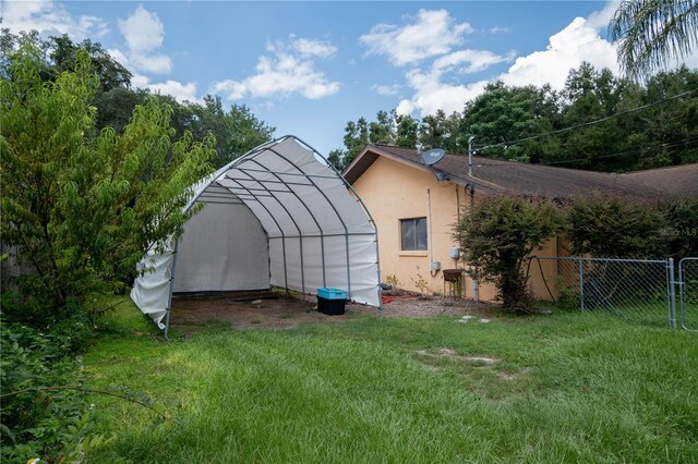 view of greenhouse with a yard, driveway, a carport, and fence