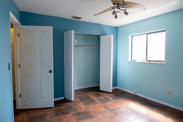 unfurnished bedroom featuring a closet, visible vents, baseboards, ceiling fan, and dark tile patterned flooring