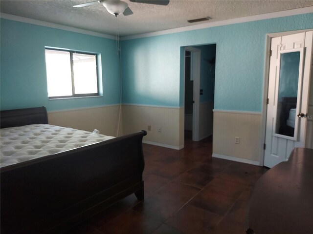bedroom featuring crown molding, a textured ceiling, visible vents, a ceiling fan, and wainscoting