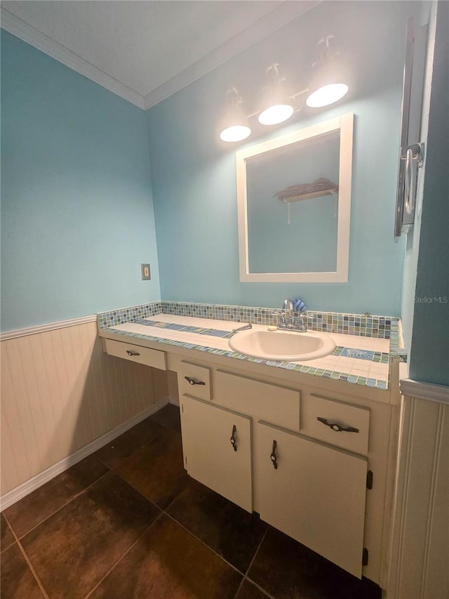 bathroom with a wainscoted wall, vanity, tile patterned floors, and crown molding