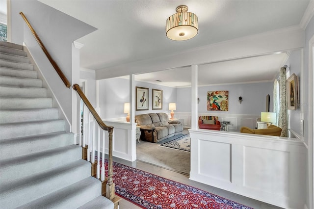 interior space featuring stairs, ornamental molding, a decorative wall, and wainscoting