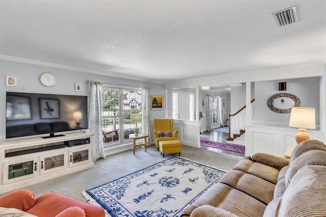 living room with a textured ceiling, light carpet, visible vents, stairway, and wainscoting