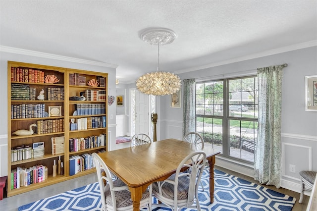 dining space with a wainscoted wall, crown molding, a textured ceiling, and wood finished floors