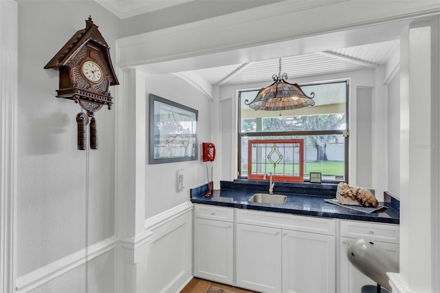 bar featuring a decorative wall, a wainscoted wall, a sink, ornamental molding, and pendant lighting