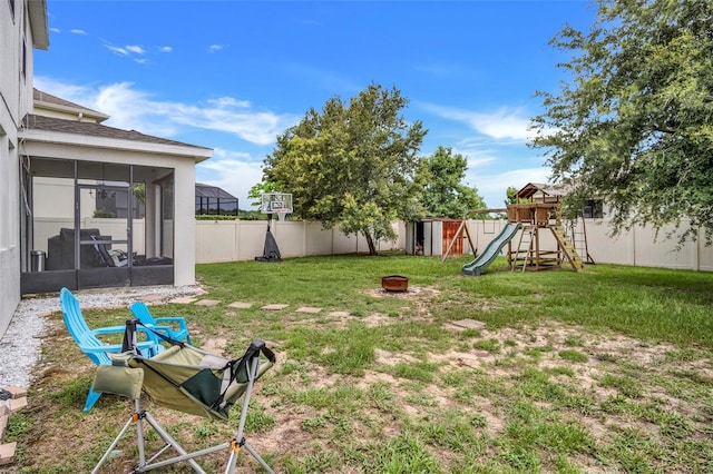 view of yard featuring a playground, a fire pit, and a sunroom