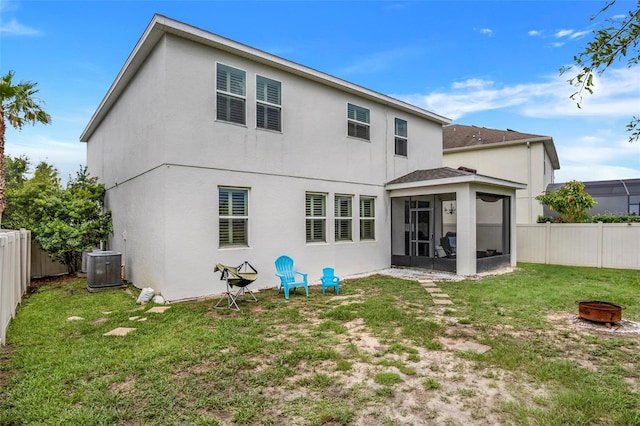 rear view of property with a fire pit, central AC unit, a lawn, and a sunroom