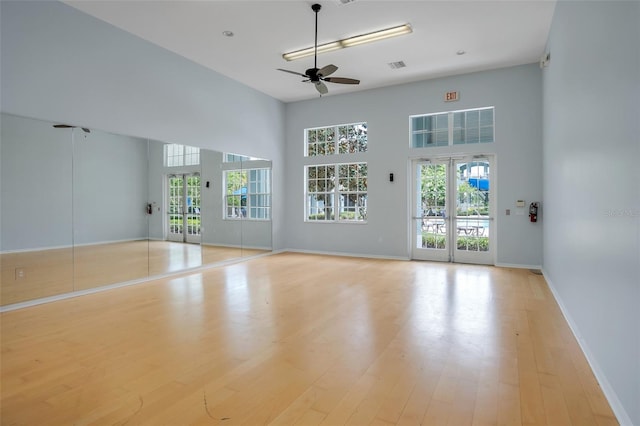 unfurnished living room featuring ceiling fan, light hardwood / wood-style flooring, a high ceiling, and french doors