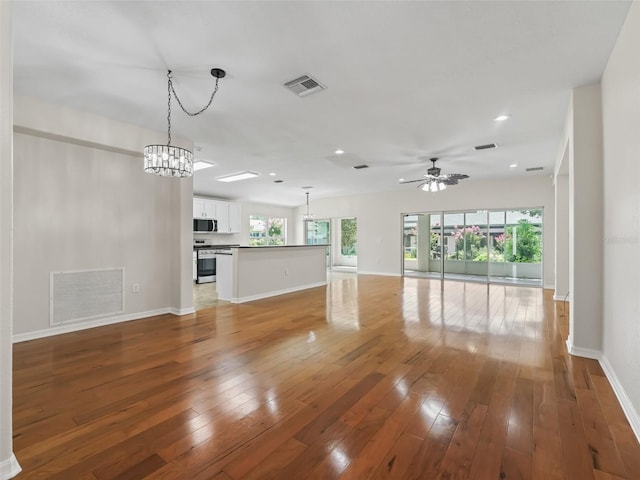 unfurnished living room with ceiling fan with notable chandelier and hardwood / wood-style flooring