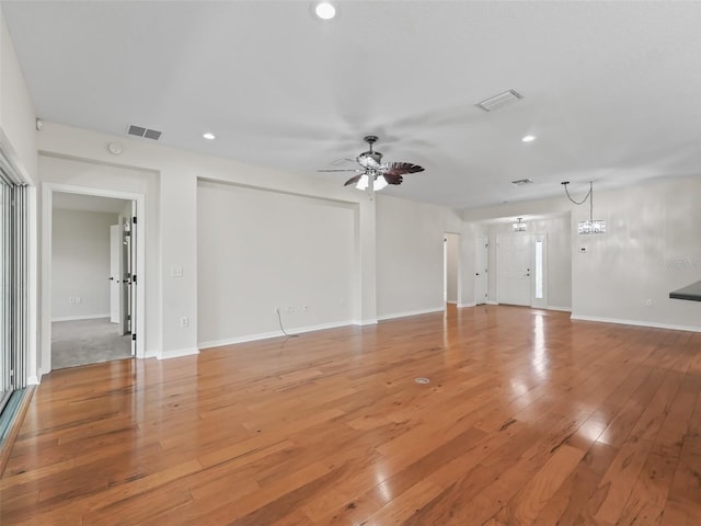 unfurnished living room featuring ceiling fan with notable chandelier and light hardwood / wood-style floors