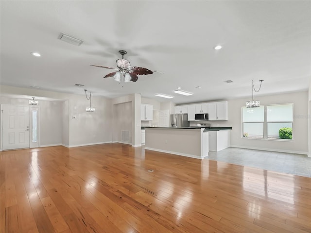 unfurnished living room featuring ceiling fan with notable chandelier and light hardwood / wood-style flooring