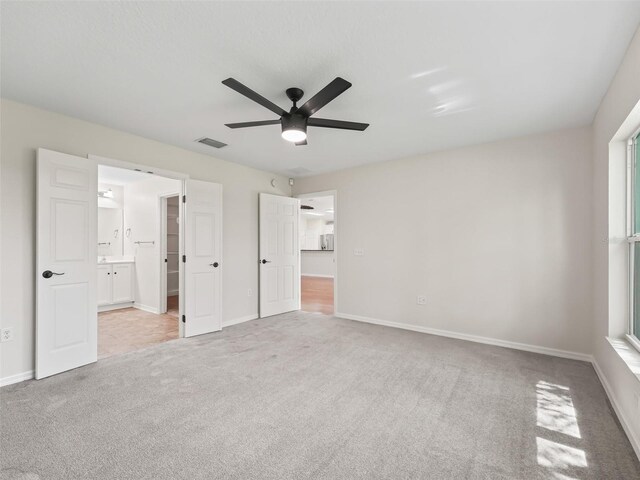 unfurnished bedroom with light carpet, ensuite bath, and ceiling fan