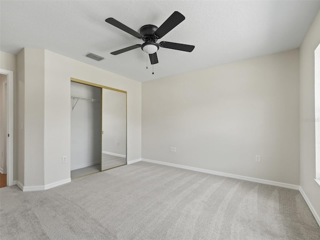 unfurnished bedroom featuring ceiling fan, light colored carpet, a textured ceiling, and a closet