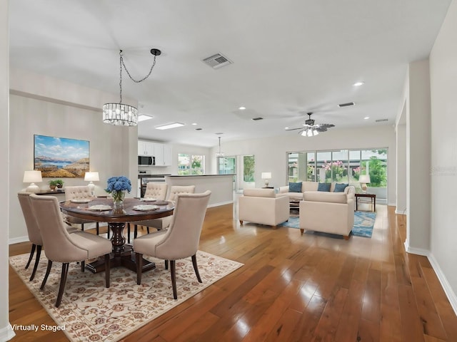 dining area with ceiling fan with notable chandelier and hardwood / wood-style flooring