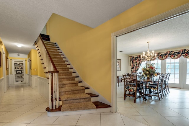 stairs featuring a notable chandelier, tile patterned floors, and a textured ceiling