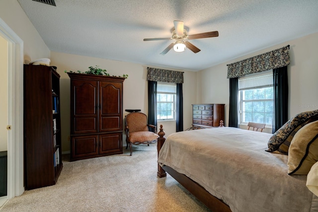 bedroom featuring a textured ceiling, light colored carpet, and ceiling fan