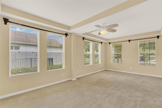 carpeted empty room with a raised ceiling, ceiling fan, and plenty of natural light