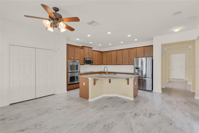 kitchen with sink, stainless steel appliances, light stone counters, a breakfast bar, and a center island with sink