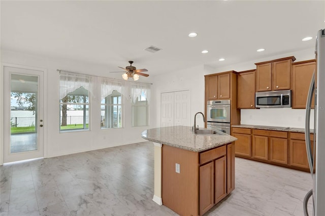 kitchen with light stone countertops, sink, ceiling fan, stainless steel appliances, and a kitchen island with sink