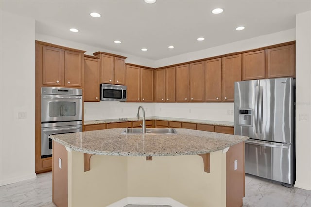 kitchen featuring a kitchen bar, a kitchen island with sink, sink, light stone counters, and stainless steel appliances