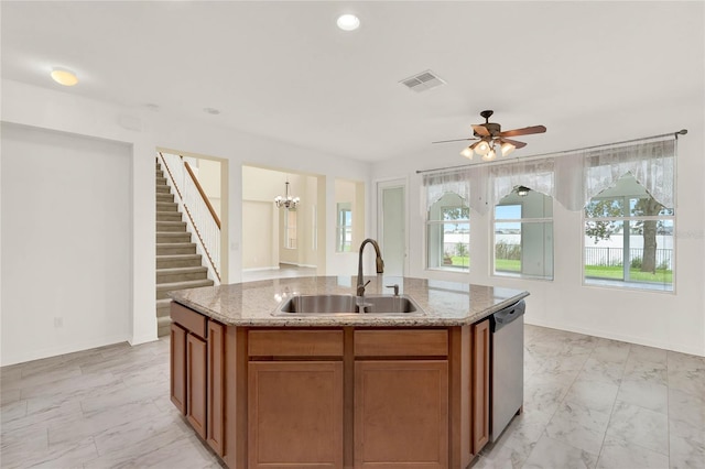 kitchen featuring dishwasher, ceiling fan with notable chandelier, sink, an island with sink, and light stone counters