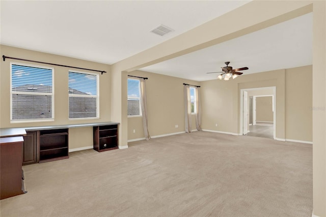 unfurnished living room with ceiling fan, light colored carpet, and built in desk