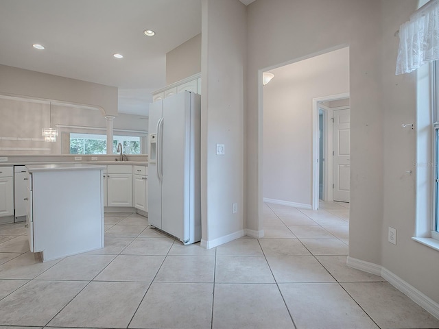 kitchen with white refrigerator with ice dispenser, sink, light tile patterned floors, a kitchen island, and white cabinetry