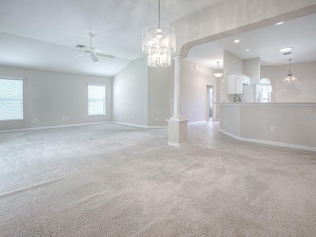 carpeted spare room featuring ceiling fan with notable chandelier, decorative columns, and vaulted ceiling