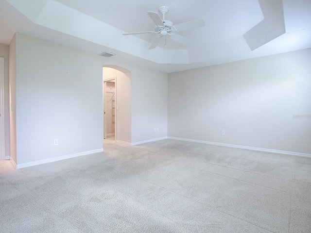 empty room with a raised ceiling, ceiling fan, and light carpet