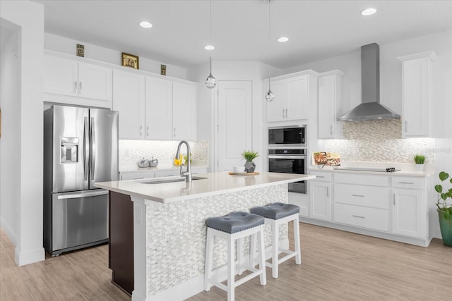 kitchen featuring sink, wall chimney range hood, appliances with stainless steel finishes, and white cabinets